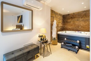 A modern bathroom with a stone wall, a large mirror, a bench, a lamp, a hot tub, and a towel rack. - AC Encanto - Relax & Comfort (Villa de Arico)
