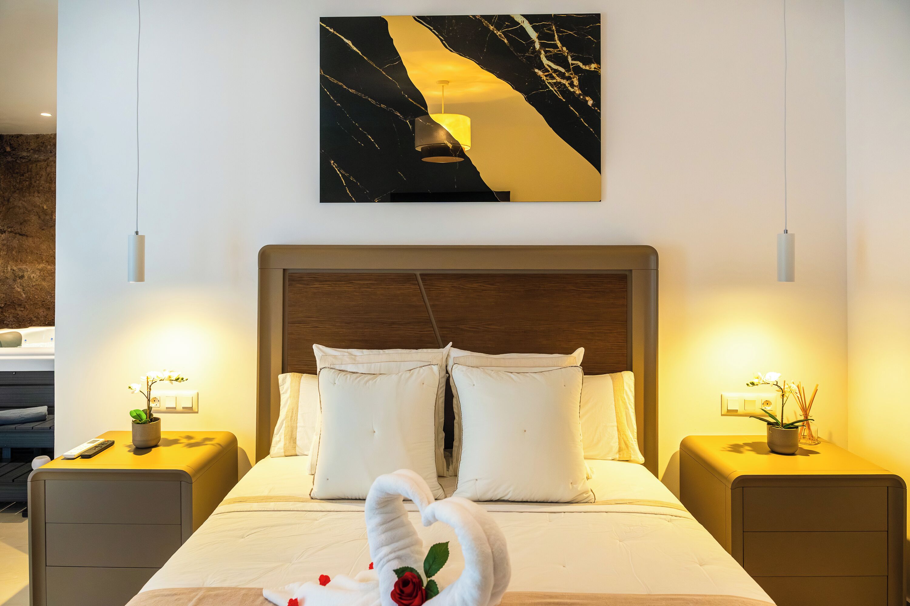 A hotel room with a bed, two bedside tables, a nightstand, a wall-mounted artwork, and a wall-mounted light fixture.