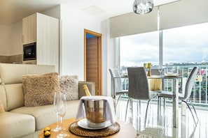 Una sala de estar moderna con un sofá, una mesa de comedor con sillas, un minibar y vistas a la ciudad.