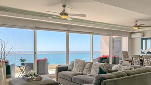 Ein geräumiges Wohnzimmer mit großem Fenster zum Meer, einem Deckenventilator und einer gemütlichen Sitzecke.