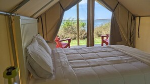 A tented accommodation with a bed, two red chairs, and a view of the sea.