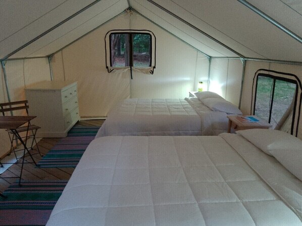 A tented accommodation with two beds, a small table, a chair, and a cabinet.