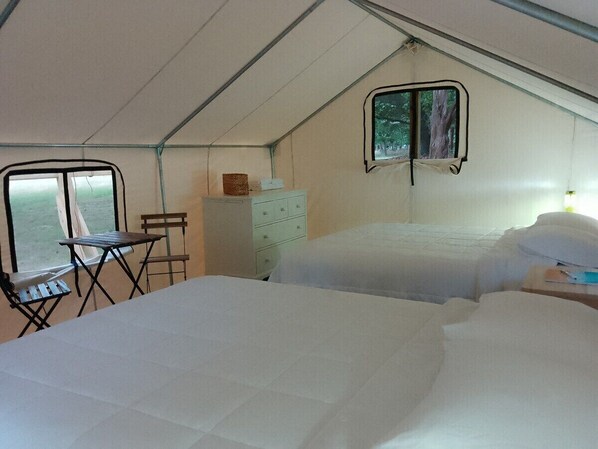 A tented room with two beds, a small table, a chair, and a dresser.