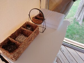 A room with a white bed, a wicker basket with toiletries, and a small mirror.