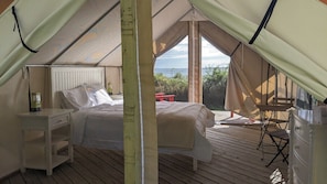 A tented accommodation with a bed, a small table, and a chair.
