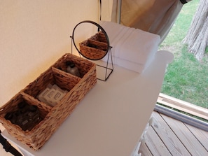 A room with a white bed, a wicker basket with toiletries, and a small mirror.