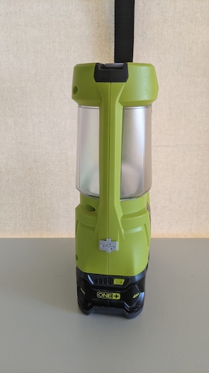 Eine tragbare Campinglaterne mit grünem Korpus und schwarzen Akzenten, mit einer transparenten Vorderseite und einem Power-Knopf.