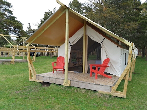 Une tente avec une structure en bois, deux chaises rouges et une table.