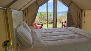 A tented accommodation with a bed, two red chairs, and a view of the sea.
