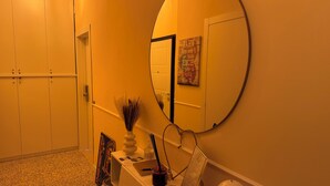 Un couloir avec un grand miroir rond, une porte et une petite table sur laquelle se trouvent un vase et une bouteille.