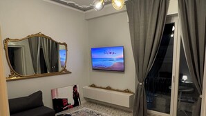 Un salon moderne doté d’un grand téléviseur à écran plat, d’un tapis à motifs, d’un canapé, d’une petite table avec une lampe et d’un luminaire au plafond.