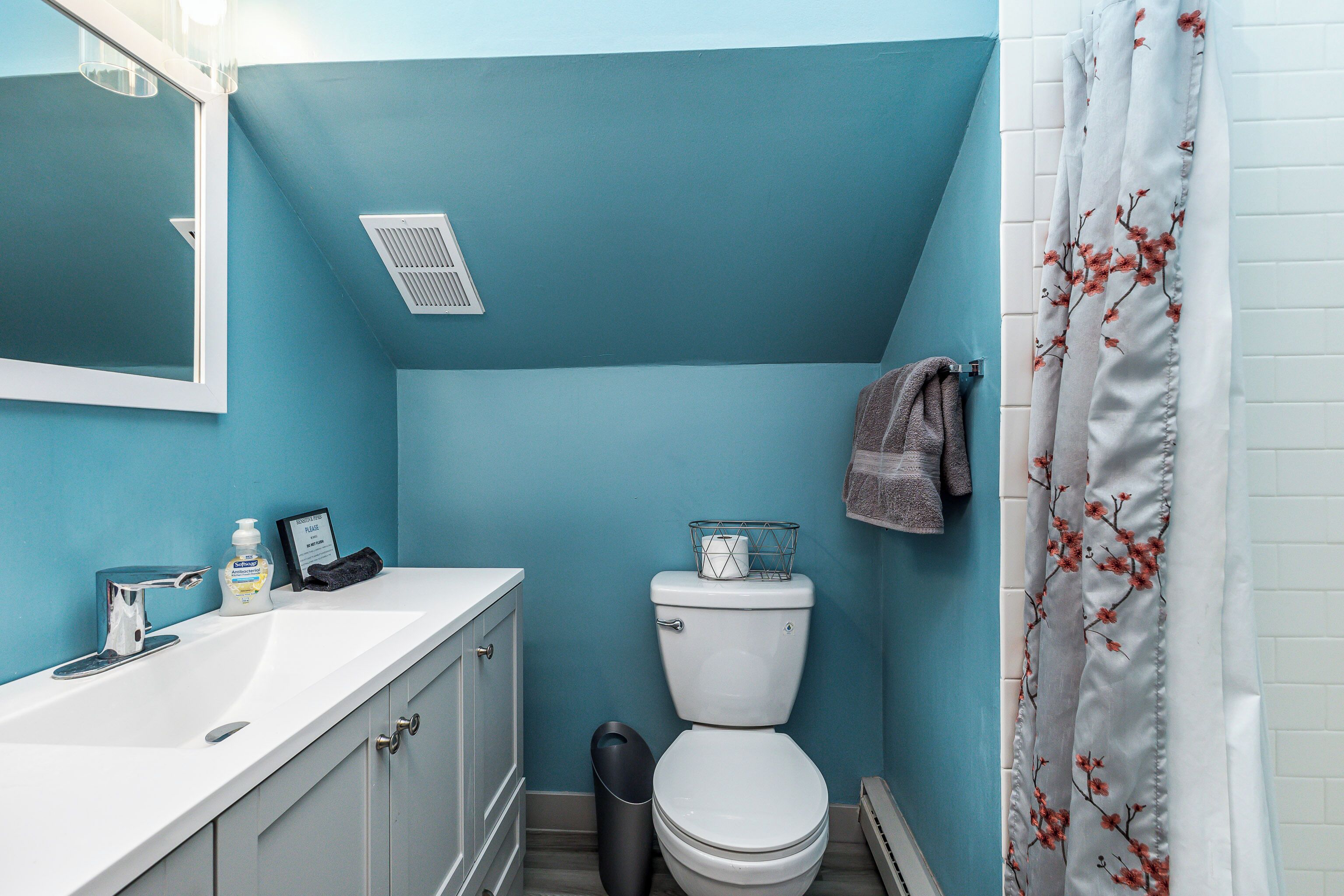 Un baño con lavamanos blanco, inodoro y cortina de ducha con motivos florales.