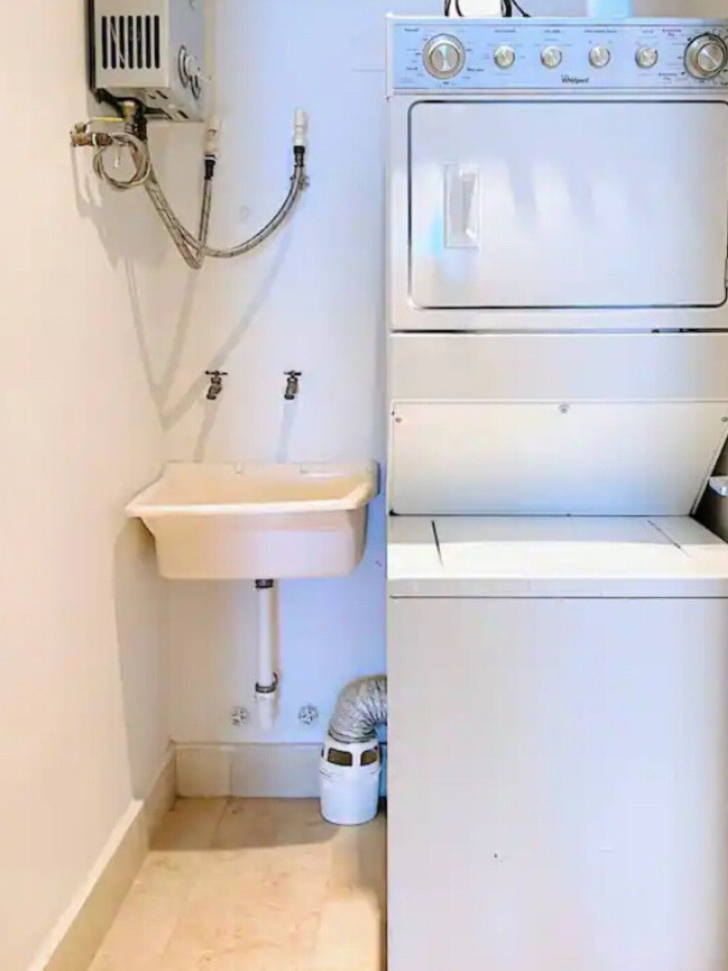 Un lavadero pequeño con lavadora y secadora integradas, un lavabo y una manguera conectada a la pared.