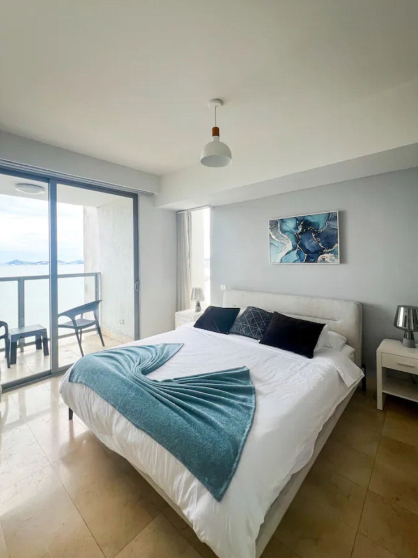 Un dormitorio moderno con una cama grande, vista al mar y un balcón con sillas.