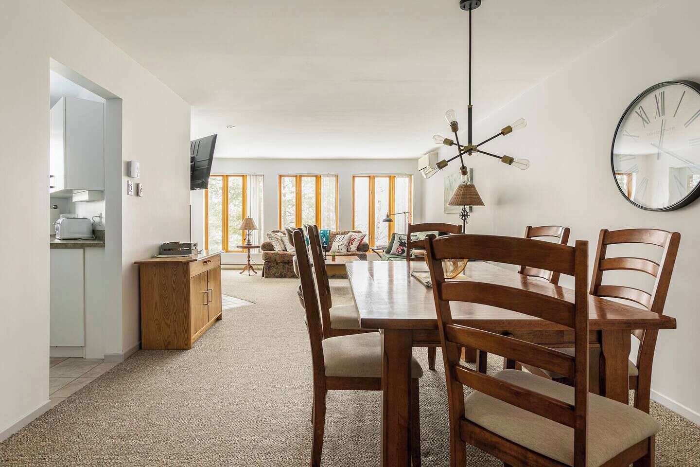 Une cuisine moderne dotée d’un four encastré, d’un coin repas avec une table et des chaises en bois, et d’une grande horloge murale.
