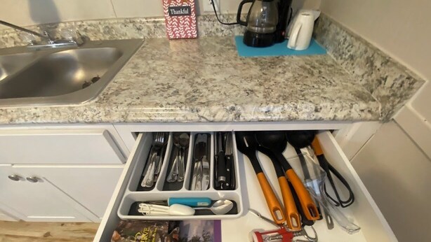 A kitchen with a granite countertop, a coffee maker, and a drawer organizer containing utensils and a picture frame.