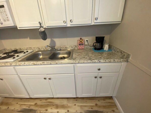 A kitchen with white cabinets, a double sink, a stove, and a coffee maker. - Come relax with nature in one of our studio cabins! (Cleveland)