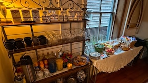 A buffet setup with various food items and drinks on a table, surrounded by shelves with kitchenware and glassware. - Lincoln Suite in charming Olinger House B&B in historic, downtown Gettysburg. (Gettysburg)