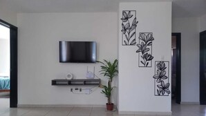 A modern living room with a flat-screen TV mounted on the wall, a small shelf with a white object, and a potted plant. - Family apartment with excellent location (Tampico)