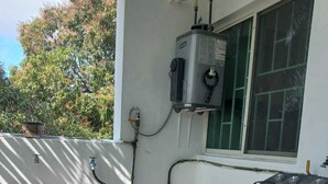 A compact laundry room with a front-loading washing machine, a water heater, and a window with a view of trees. - Family apartment with excellent location (Tampico)