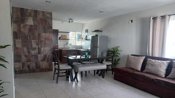 A living room with a sofa, a dining table with chairs, a kitchen area with a refrigerator, and a stone accent wall. - Family apartment with excellent location (Tampico)