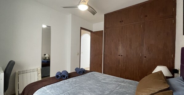 A bedroom with a large bed, a wooden wardrobe, a ceiling fan, and a radiator.