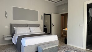 Une chambre à coucher comprenant un lit, des tables de chevet, un banc, un miroir et une porte donnant sur une autre pièce.