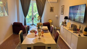 Un coin repas avec une table dressée pour quatre personnes, agrémenté d’un vase de fleurs, d’un plateau de fruits et de verres décoratifs.