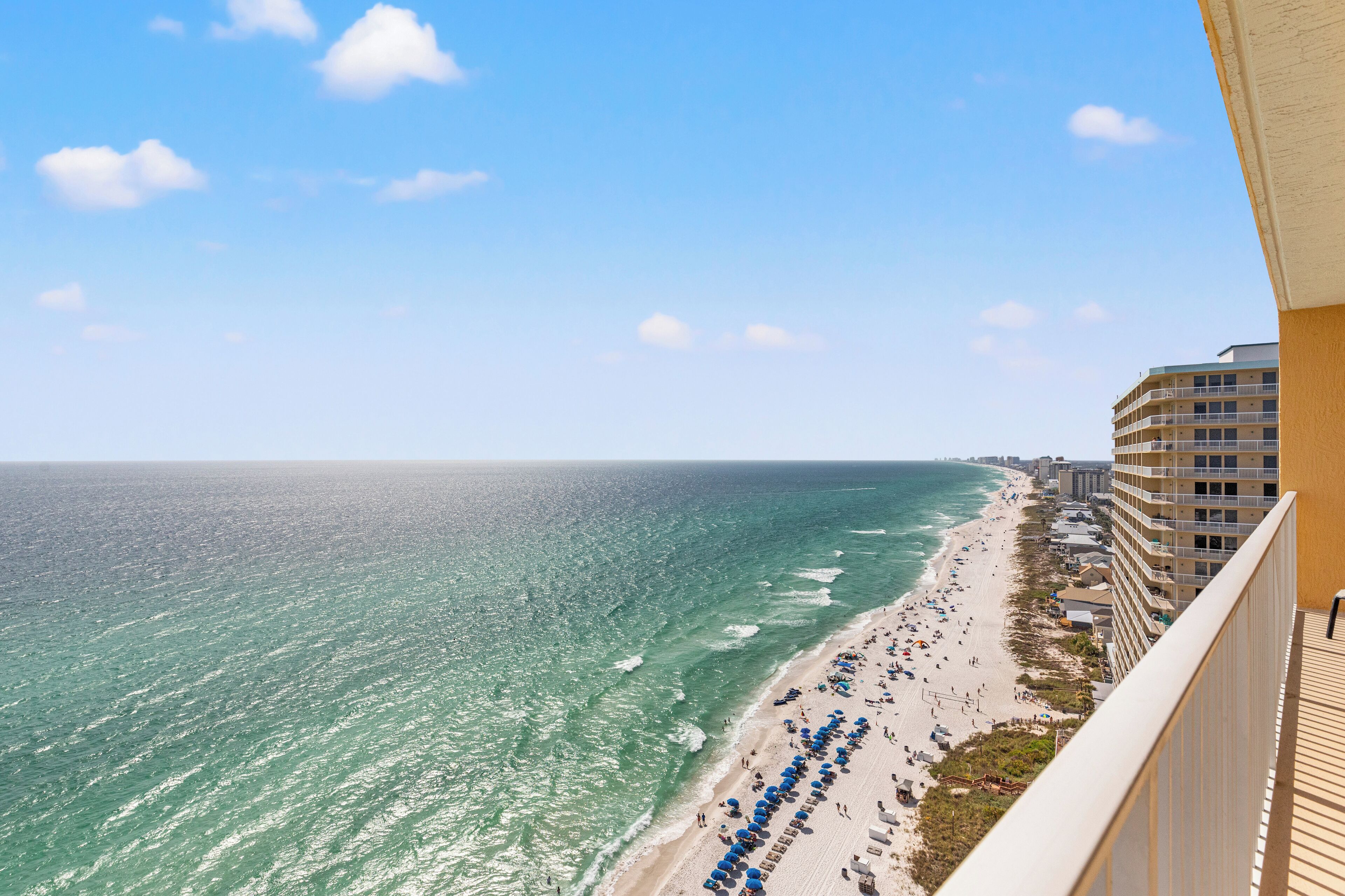 Une vue sur la plage depuis un balcon donnant sur une plage de sable, avec des parasols et un bâtiment d'hôtel en arrière-plan.