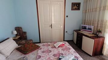 A bedroom with a bed, a wooden headboard, a wardrobe, a desk with a computer, and a curtain.