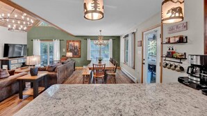 A spacious living room with a large TV, a fireplace, and a dining area with a wooden table and chairs. - Emerald Bliss, MiniGolf Bowling Playset Beach Horseshoe Cornhole (Towamensing Trails)