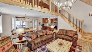 A spacious living area with a high ceiling, a staircase, and a kitchen in the background. - Emerald Bliss, MiniGolf Bowling Playset Beach Horseshoe Cornhole (Towamensing Trails)
