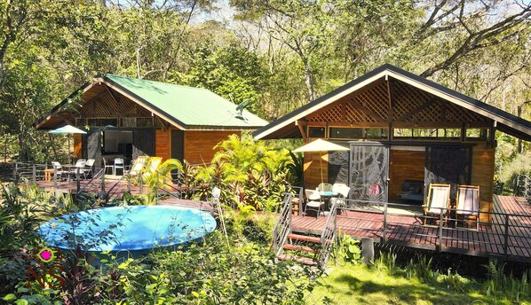 Two wooden cabins with green roofs, a pool, and outdoor seating.
