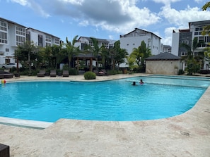 A swimming pool with lounge chairs and a gazebo, surrounded by buildings and palm trees.