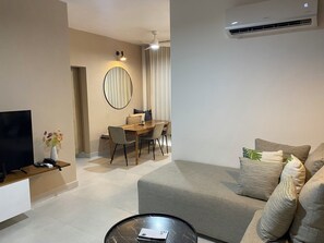 Ein modernes Wohnzimmer mit Sofa, Couchtisch, Fernseher, Essbereich mit Tisch und Stühlen sowie Deckenventilator.
