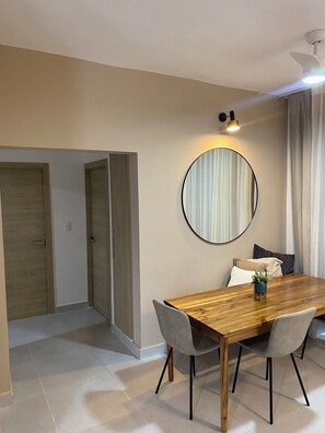 A dining area with a wooden table, chairs, a round mirror, and a ceiling fan. - EXPECTACULAR APARTAMENT DE 2 HABITACIONES (Las Terrenas)