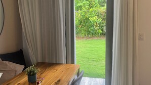 A dining area with a wooden table and chairs, a small plant, and a view of a green garden through a sliding door. - EXPECTACULAR APARTAMENT DE 2 HABITACIONES (Las Terrenas)