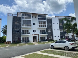 A multi-story residential building with balconies, a covered entrance, and a car parked in front. - EXPECTACULAR APARTAMENT DE 2 HABITACIONES (Las Terrenas)