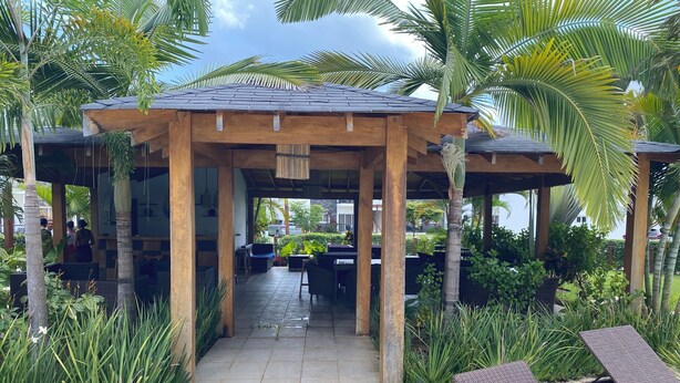 A covered outdoor seating area with tables and chairs, surrounded by lush greenery and palm trees. - EXPECTACULAR APARTAMENT DE 2 HABITACIONES (Las Terrenas)