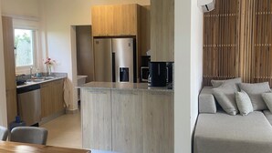 A modern kitchen with wooden cabinets, a built-in fridge, and a coffee machine. There is a dining area with a wooden table and chairs. - EXPECTACULAR APARTAMENT DE 2 HABITACIONES (Las Terrenas)