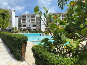 A swimming pool surrounded by greenery, with a building in the background. - EXPECTACULAR APARTAMENT DE 2 HABITACIONES (Las Terrenas)
