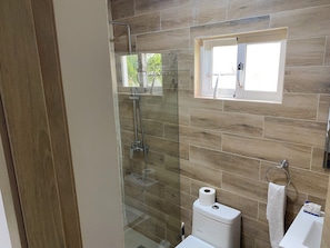 A bathroom with a glass-enclosed shower, a toilet, and a window above the sink.