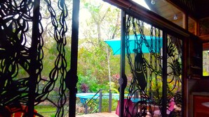 Una habitación con vista a una terraza de madera y follaje exterior, una reja de metal y una lámpara del techo.