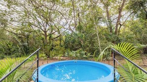 Piscina al aire libre con terraza de madera y barandillas metálicas, rodeada de exuberante vegetación.