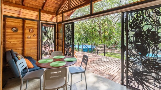 Interior de madera con comedor, sofá y vista a una piscina exterior.