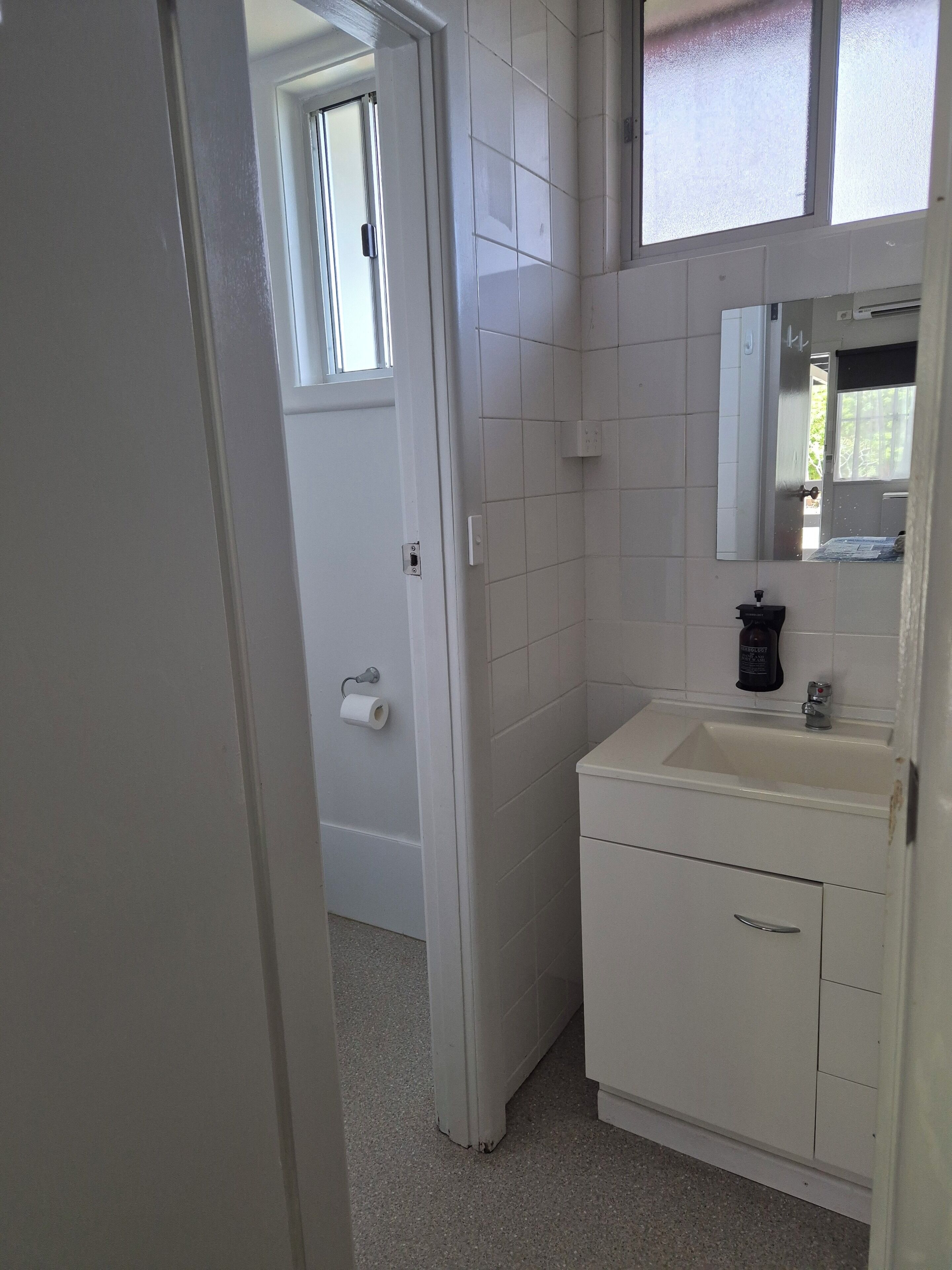A bathroom with white tiles, a sink, a mirror, and a toilet.