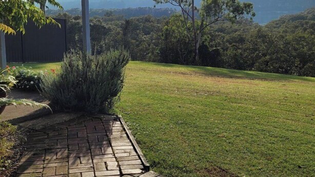 A paved pathway leading to a covered area with a view of a grassy landscape and trees. - Jabiru Motel (Nambucca Heads)