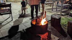 An outdoor patio area with a fire pit, seating, and a covered section with a metal roof. - Jabiru Motel (Nambucca Heads)
