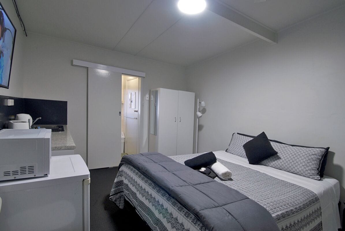 A hotel room with a bed, a desk with a computer, a wardrobe, and a door leading to another room.
