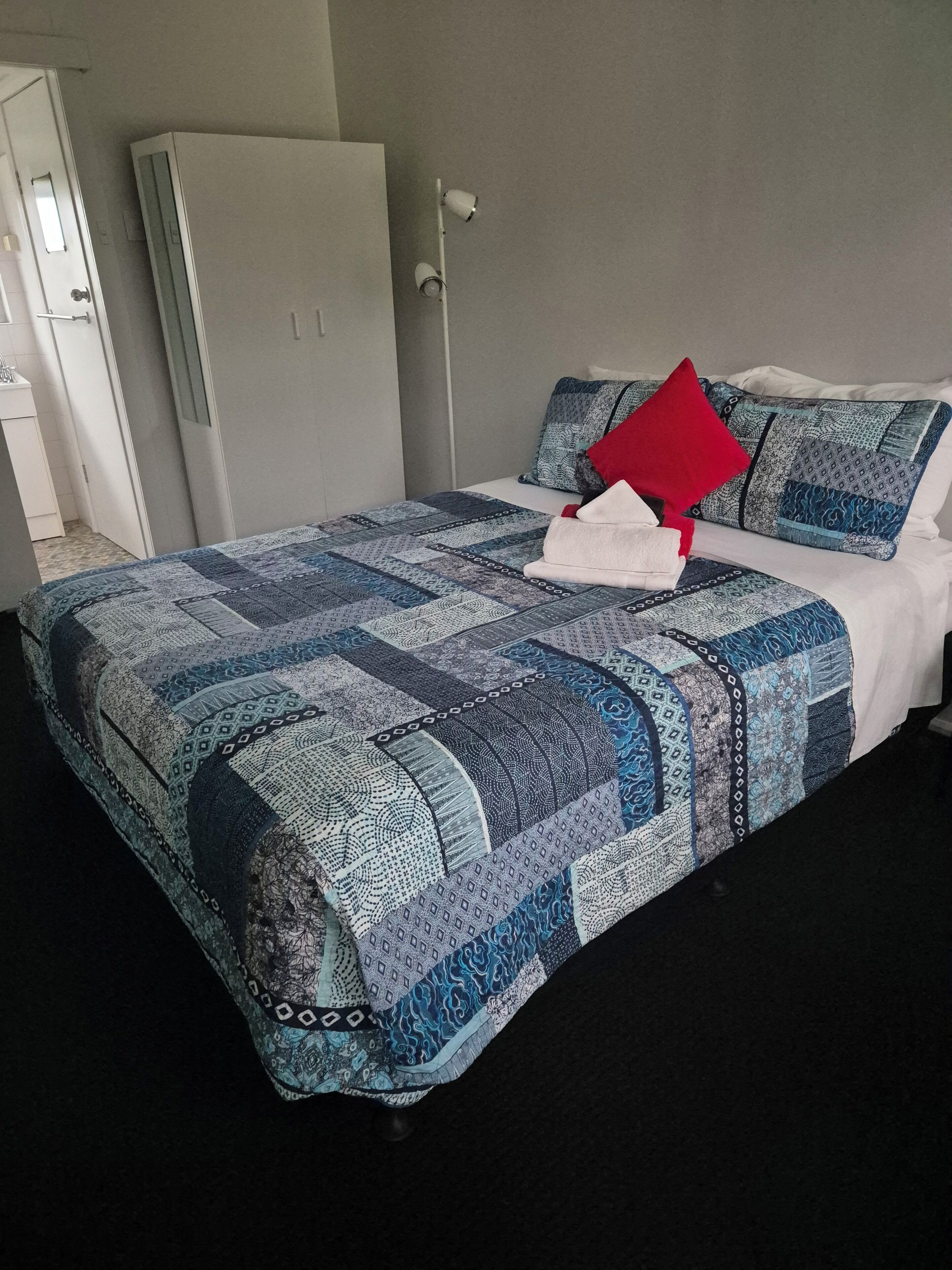 A neatly made bed with a blue and white patterned bedspread, a red pillow, and a white pillow.